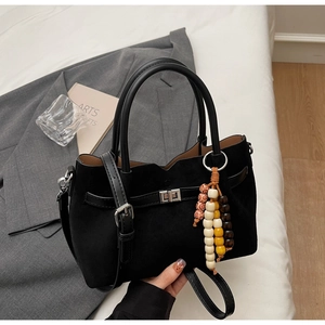 Détail du sac seau en daim noir avec poignées rondes et gland en perles de bois