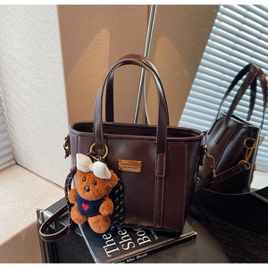 Detail of dark brown leather bucket bag with gold fashion plate and cute teddy bear charm