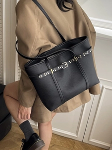Chic black lychee leather tote bag with gold buckle and rivets worn by female model
