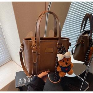 Detail view of deep brown pebbled tote with golden plaque and teddy bear charm accessory