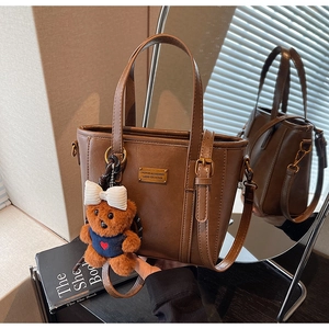 Detail view of brown PU leather bucket bag with golden metal tag and cute plush bear charm