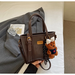 Detail of vintage brown tote bag with metal plaque, teddy bear charm and silk scarf