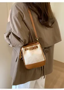 Detail of a minimalist two-tone bucket bag with wooden bead charm and brown leather straps