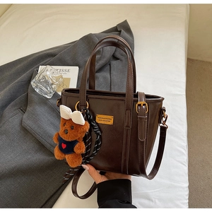Detailed side view of vintage dark brown leather tote bag with cute bear charm on white bed