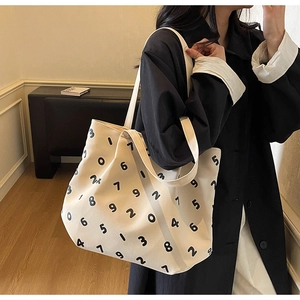 Close-up of cream canvas tote bag with black numeric print on a shoulder-carried model