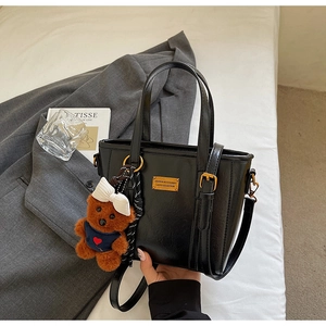 Detail of black faux leather tote bag with gold logo plate and cute teddy bear charm