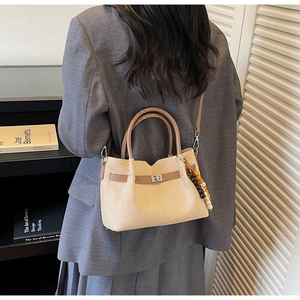 Gros plan d'un sac seau en daim crème avec poignées brunes et charms sur mannequin