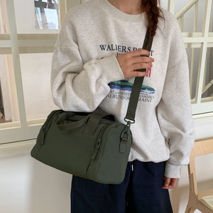 Dettaglio della borsa a cilindro verde scuro con ampi manici in nylon e ganci in metallo