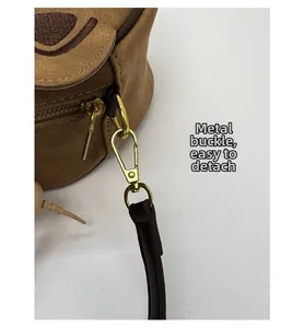 Gros plan du fermoir en métal doré et du tissu en daim sur le sac à bandoulière marron