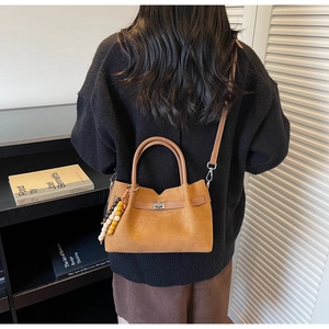 Detalle de un bolso Boston de ante marrón con correas de cuero y colgante de madera