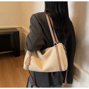 Detail of beige suede shoulder bag with dark brown leather trim and golden logo tag