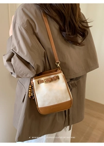 Detail of minimalist bucket bag featuring contrast leather trim and beaded tassel charm