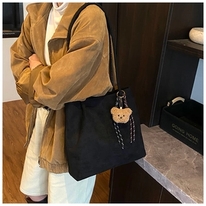 Detail of a large black suede tote bag featuring a cute bear charm for daily commuting