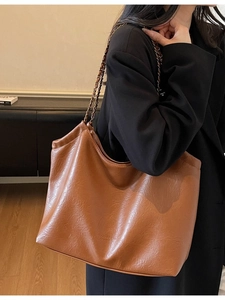 Brown leather hobo tote bag with chain strap worn by a model in a black suit