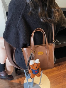 Vintage brown leather tote bag with bear charm shown on model in a cozy indoor setting