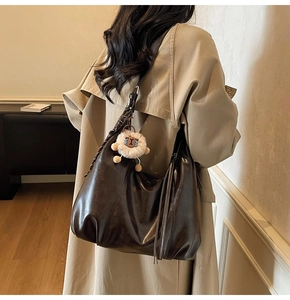 Detail of dark brown glossy leather tote bag with a white plush sheep charm pendant