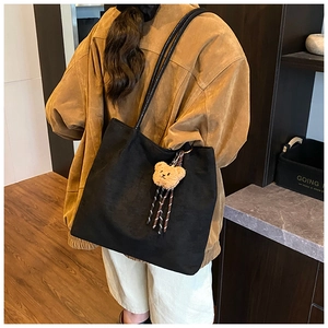 Detail of a black matte tote bag worn by a model, featuring a brown teddy bear pendant