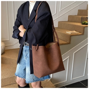 Große braune Wildleder-Eimertasche an einem Model in einem modernen, urbanen Ambiente