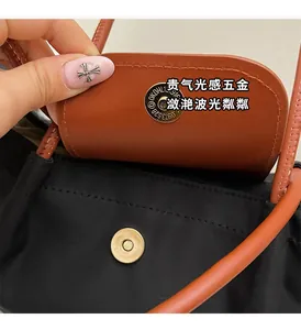 Close-up of golden snap button and brown leather flap on black nylon tote bag
