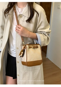 Close-up of minimalist bucket bag in cream and brown with beaded tassel and strap detail