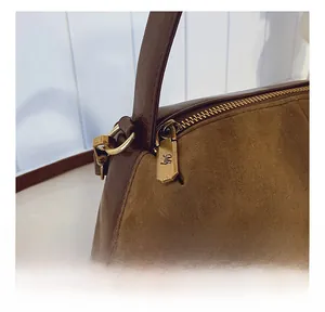 Close-up of golden MJ metal zipper puller on luxury leather and suede boston bag