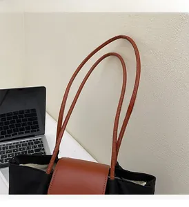 Close-up of durable brown leather handle on a minimalist black canvas tote bag