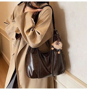 Detail of dark brown vintage tote bag with plush charm on a khaki trench coat