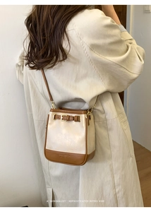 Detail of minimalist bucket bag in beige and brown leather being worn with a trench coat