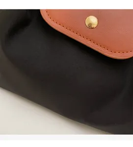 Detail of high-density black nylon fabric with brown leather flap and gold snap button