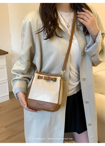Detail of minimalist cream and brown leather bucket bag with strap and belt buckle