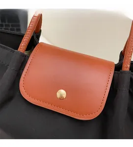 Close-up of black nylon tote bag featuring brown leather flap and gold metal snap button