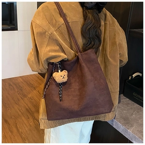 Detail of a large brown suede tote bag with a cute bear charm and woven rope knot