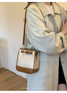 Detailed view of cream and brown crossbody bag with metal buckle on beige coat