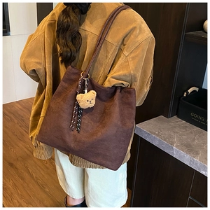 Detail of dark brown vintage tote bag featuring a plush bear pendant and cord decoration