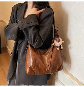 Side view of vintage brown leather hobo bag with fringe zipper and plush charm on shoulder