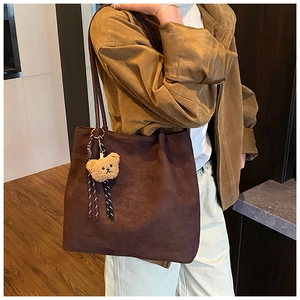 Detail view of large brown suede tote bag with a cute teddy bear charm on the shoulder