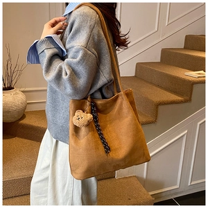 Detail of a large brown tote bag featuring a plush bear charm and textured ribbon accent