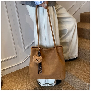 Detailed shot of a brown suede tote bag with a cute bear charm on a staircase
