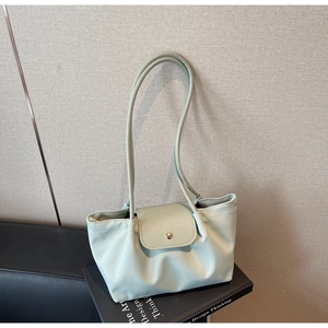 Mint green faux leather tote bag with magnetic flap closure resting on a black book