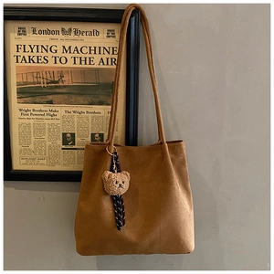 Detailed macro of brown suede tote bag featuring a cute beige plush bear pendant