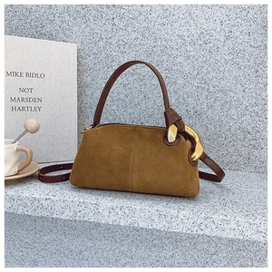 Detailed macro view of a brown suede shoulder bag featuring a bold chunky gold chain link