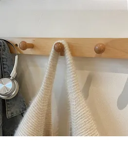Detail view of the wide shoulder strap on a fuzzy beige knit tote bag hung on a wooden hook