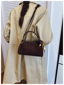 Detail view of dark coffee suede crossbody bag with artistic gold metal handle on beige coat