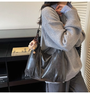 Close-up of large black leather tote with a pink plush charm on the shoulder strap