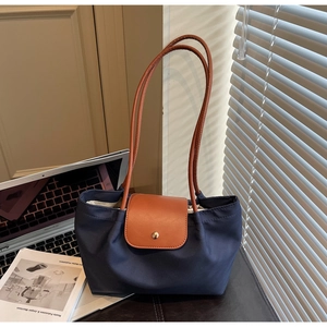 Detail of navy tote bag with brown leather flap and gold snap on a desk with laptop
