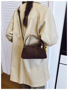 Detail of a dark brown suede crossbody bag with distinctive gold hardware and slim strap