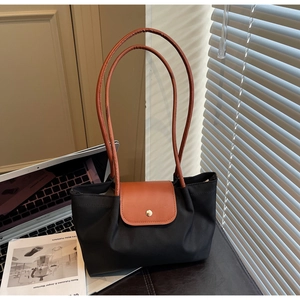 Detail of black nylon tote bag featuring brown leather straps and gold snap closure