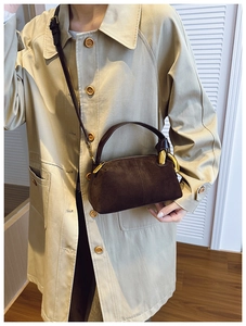 Detail of dark brown suede crossbody bag with gold hardware worn on beige trench coat