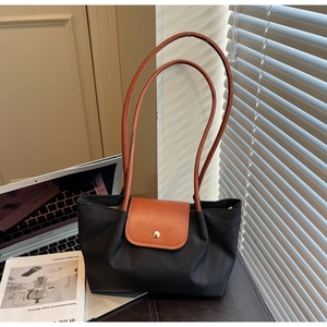 Detail of minimalist black nylon tote bag with brown leather straps in office setting