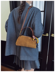 Detailed close-up of brown suede luxury shoulder bag with premium gold horseshoe hardware buckle